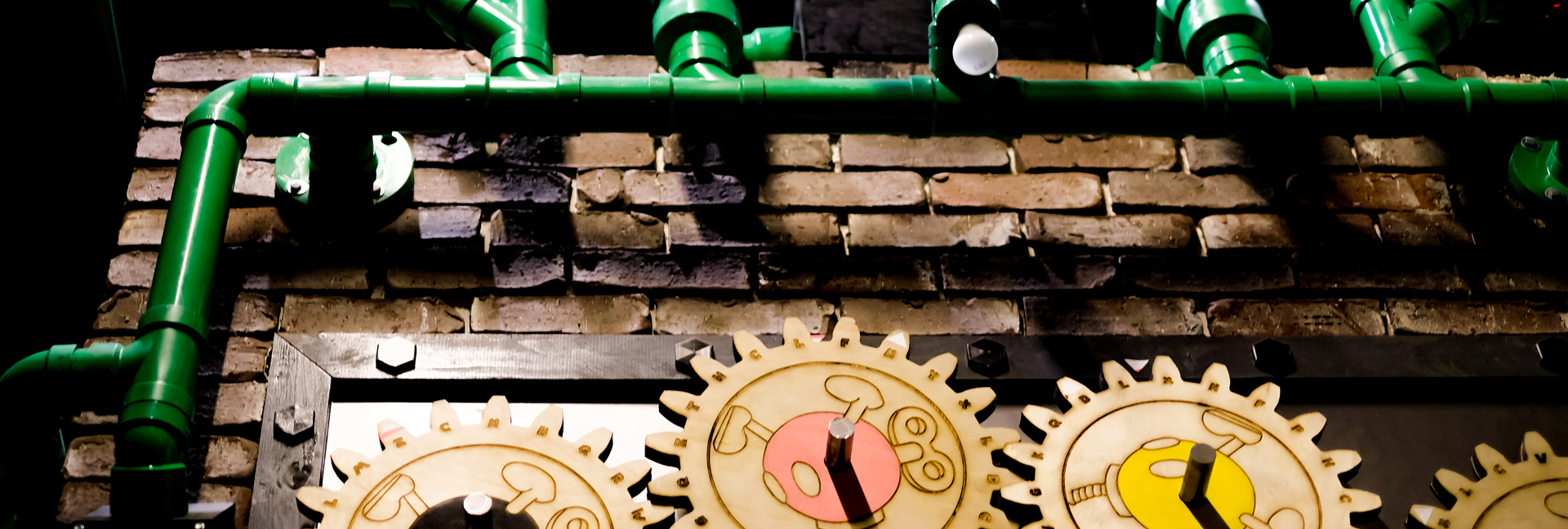 Green pipes and wooden gears on brick wall.